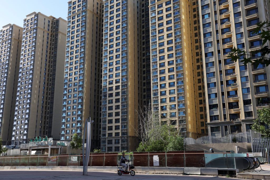 A woman rides a scooter past residential buildings at an Evergrande residential complex in Beijing