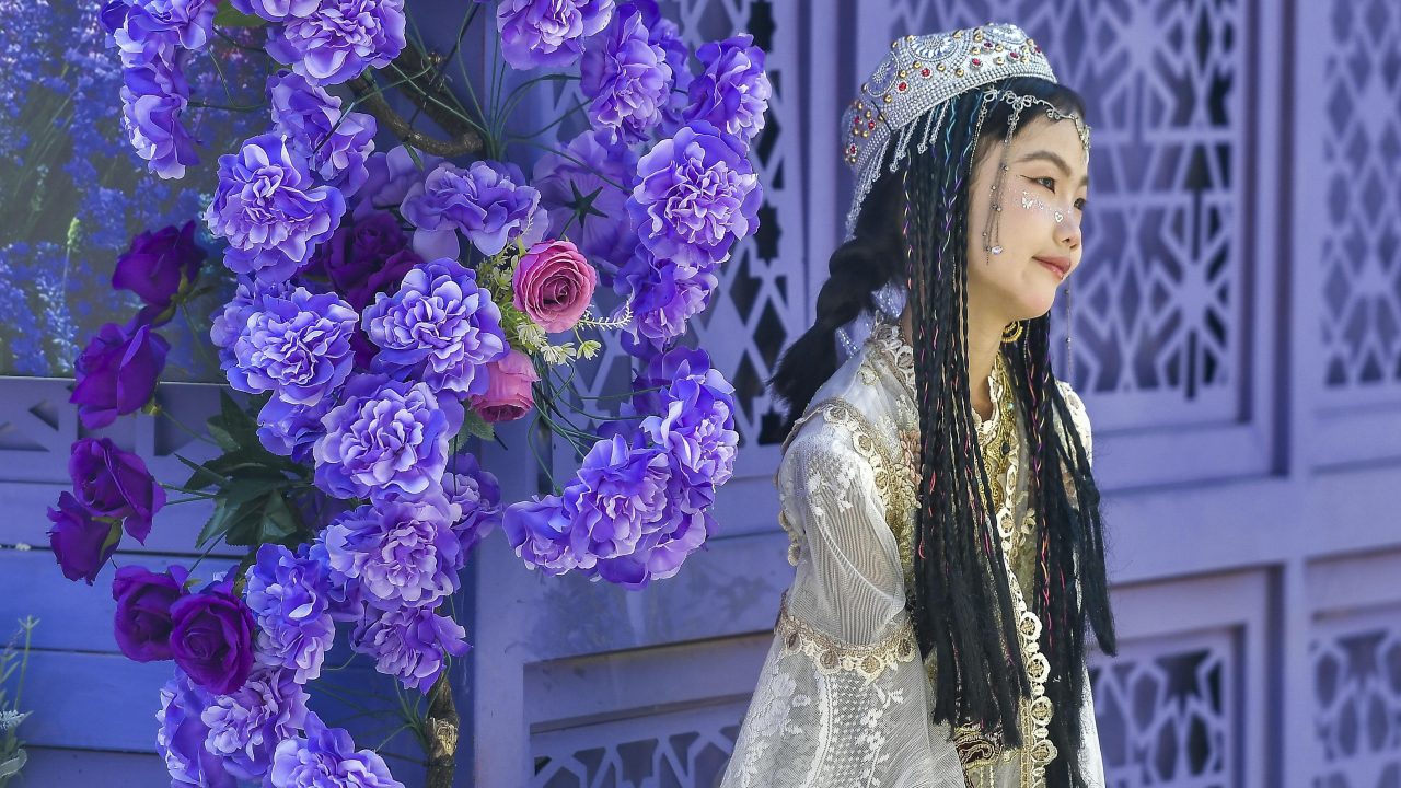 A tourist in traditional Uyghur dress poses for photos at Xinjiang International Grand Bazaar in Urumqi, Xinjiang’s capital, on August 12. (Photo: Oriental Image via Reuters Connect)