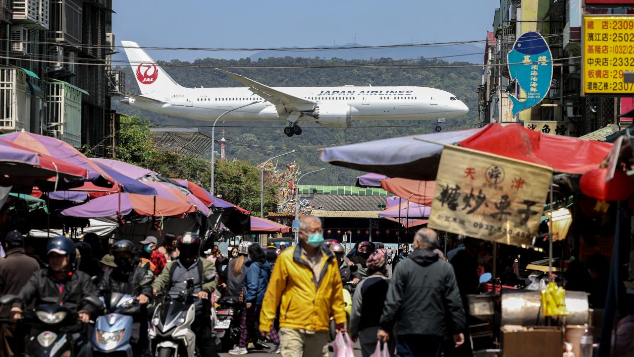 A Japan Airlines passenger plane lands as people visit a market in Taipei on March 20. (Photo by I-Hwa Cheng: AFP)